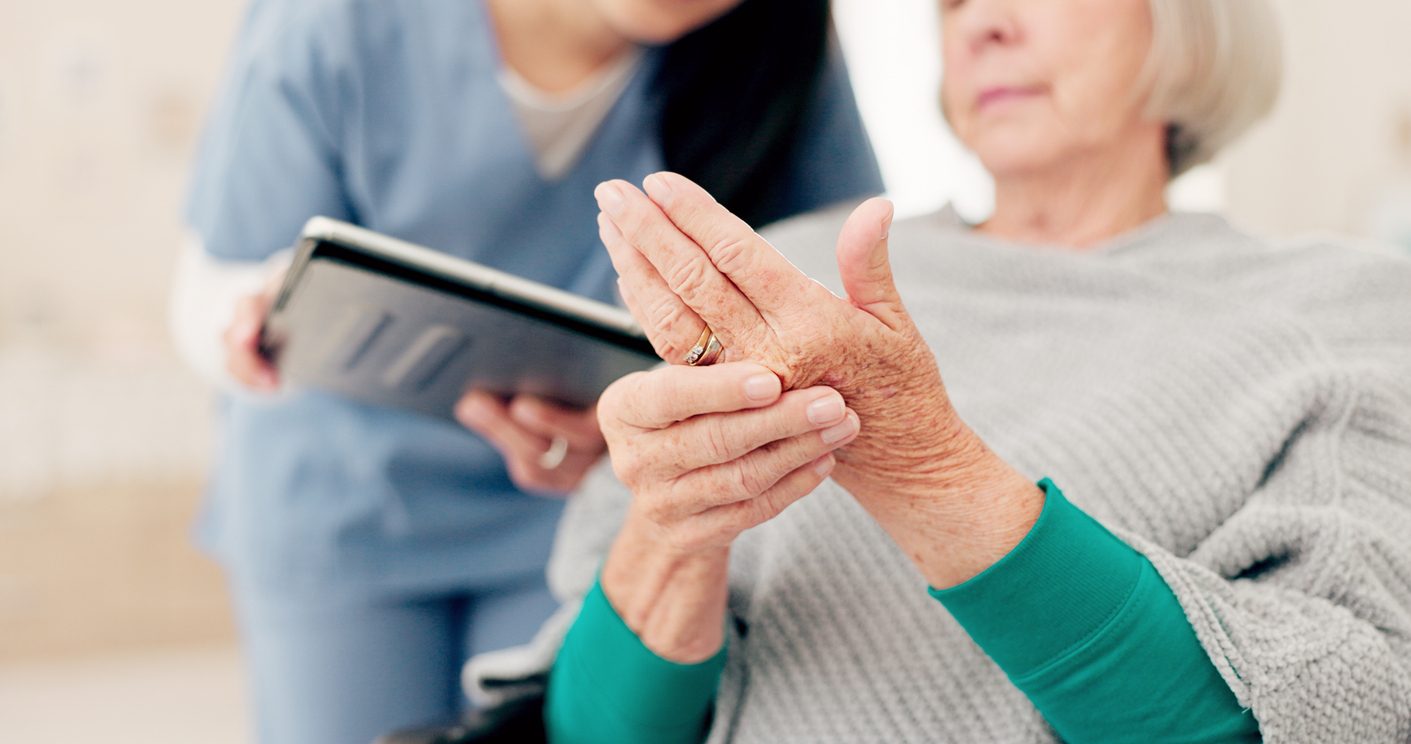 Healthcare professional using tablet to consult electronic records and elderly patient holding painful hands