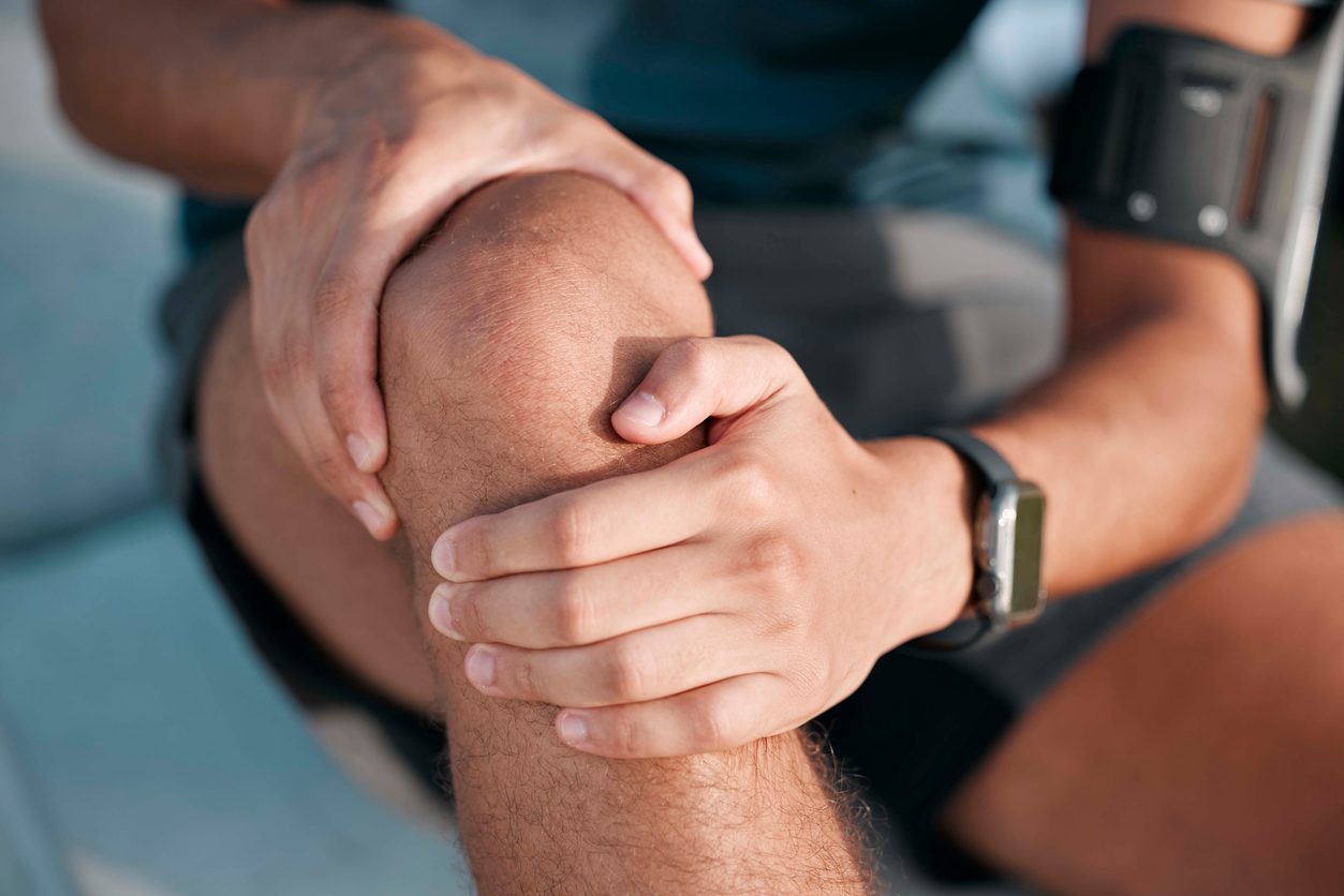 Man wearing running gear and fitness watch holding painful knee