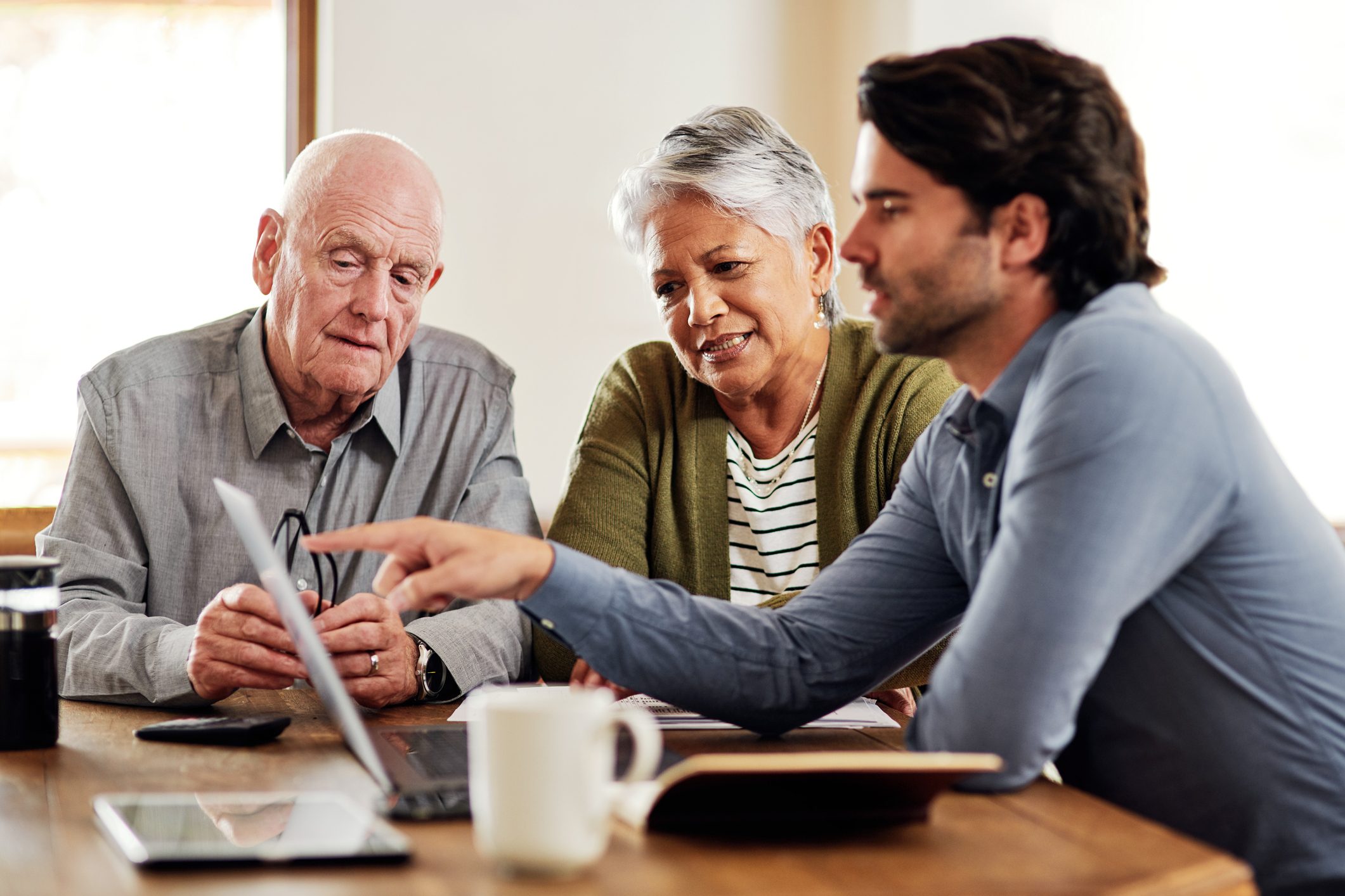 Two older people look at a laptop, whilst a younger man points to the screen
