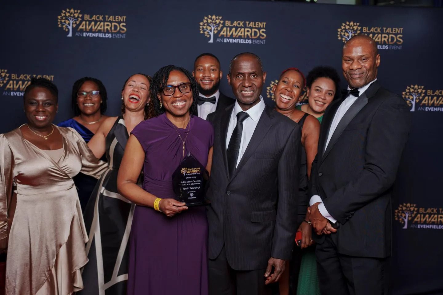 Yemisi holding her prize surrounded by a group of smiling people in 'black tie' clothing.