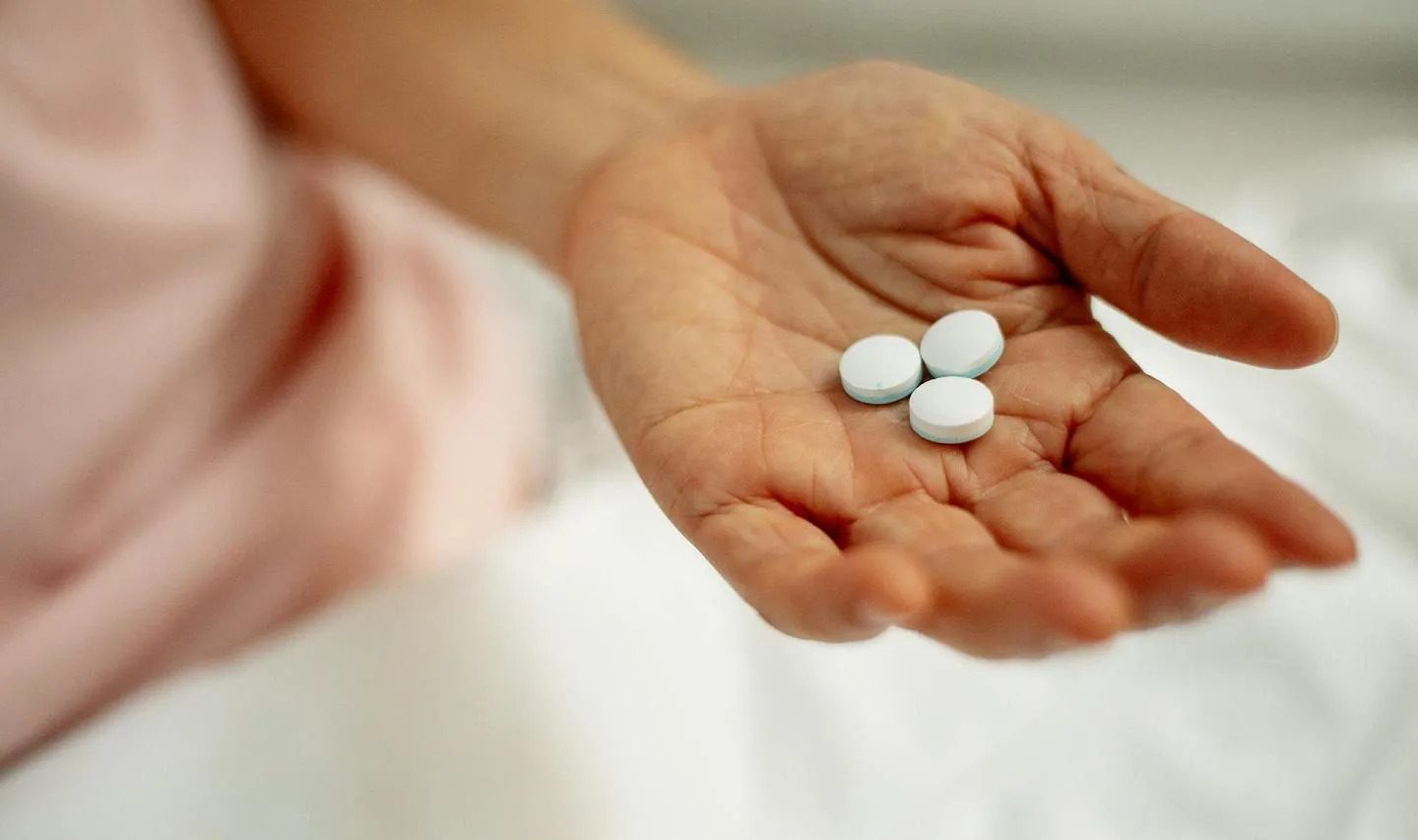 Woman's hand holding three white medicine pills