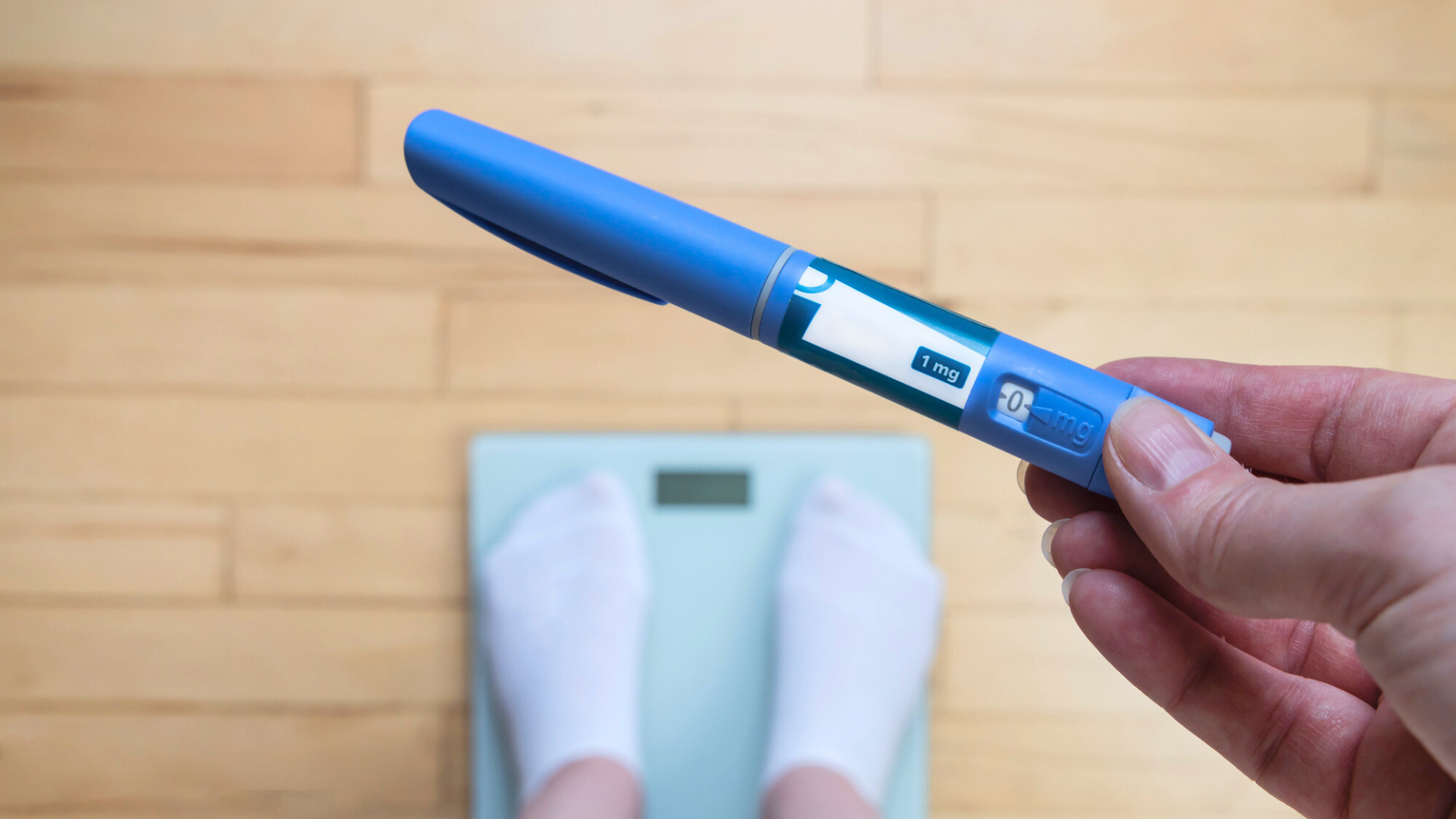 Person weighing themselves on a scale while holding an injector pen for a weight loss drug